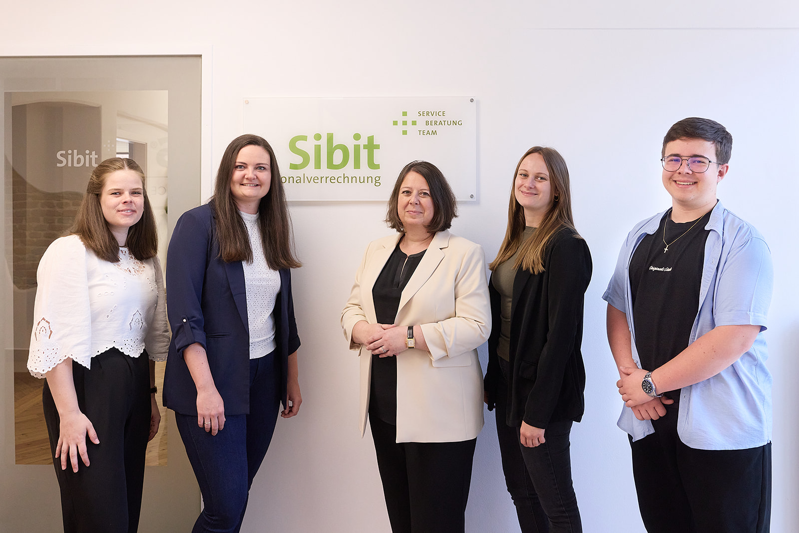 Fünf Mitglieder des SIBIT-Teams stehen gemeinsam vor dem Firmenschild im Büro.