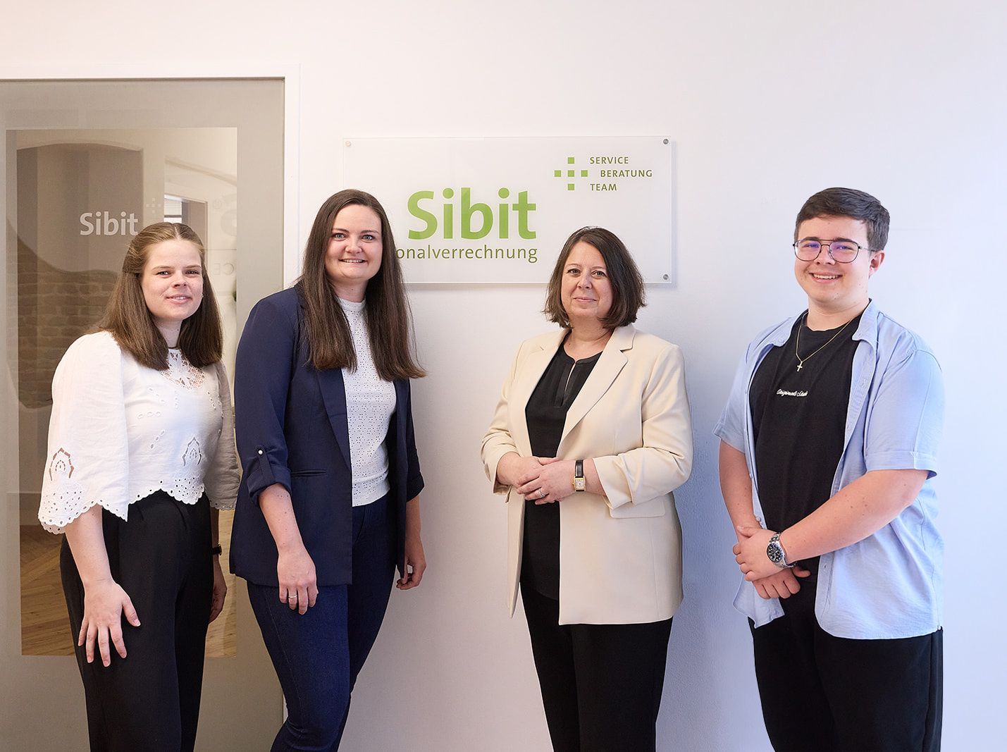 Vier Mitglieder des SIBIT-Teams stehen gemeinsam vor dem Firmenschild im Büro.